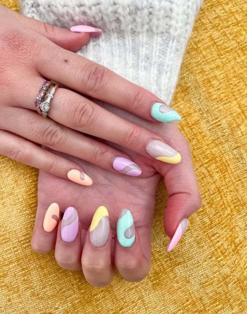 Manos de mujer con uñas acrílicas almendradas de color beige y diseños de uñas garabateados en colores pastel.