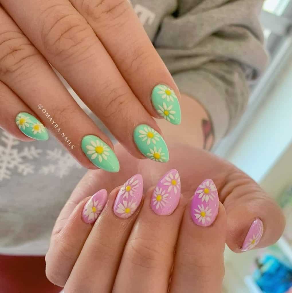 Un primer plano de las manos de una mujer con uñas acrílicas en forma de almendra en verde por un lado y rosa por el otro que tiene diseños de uñas en forma de margaritas.