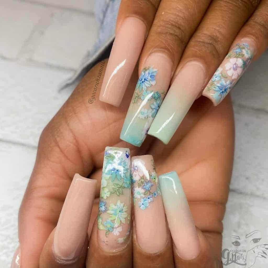 Un primer plano de las manos de una mujer con uñas largas que combinan el color nude y el verde menta con diseños de uñas con estampados de flores blancas y azules.
