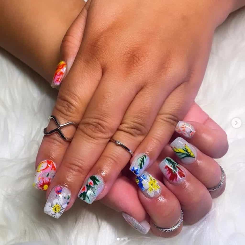 Manos de mujer con esmalte de uñas acrílico de color plateado brillante que tiene diseños de uñas de flores.